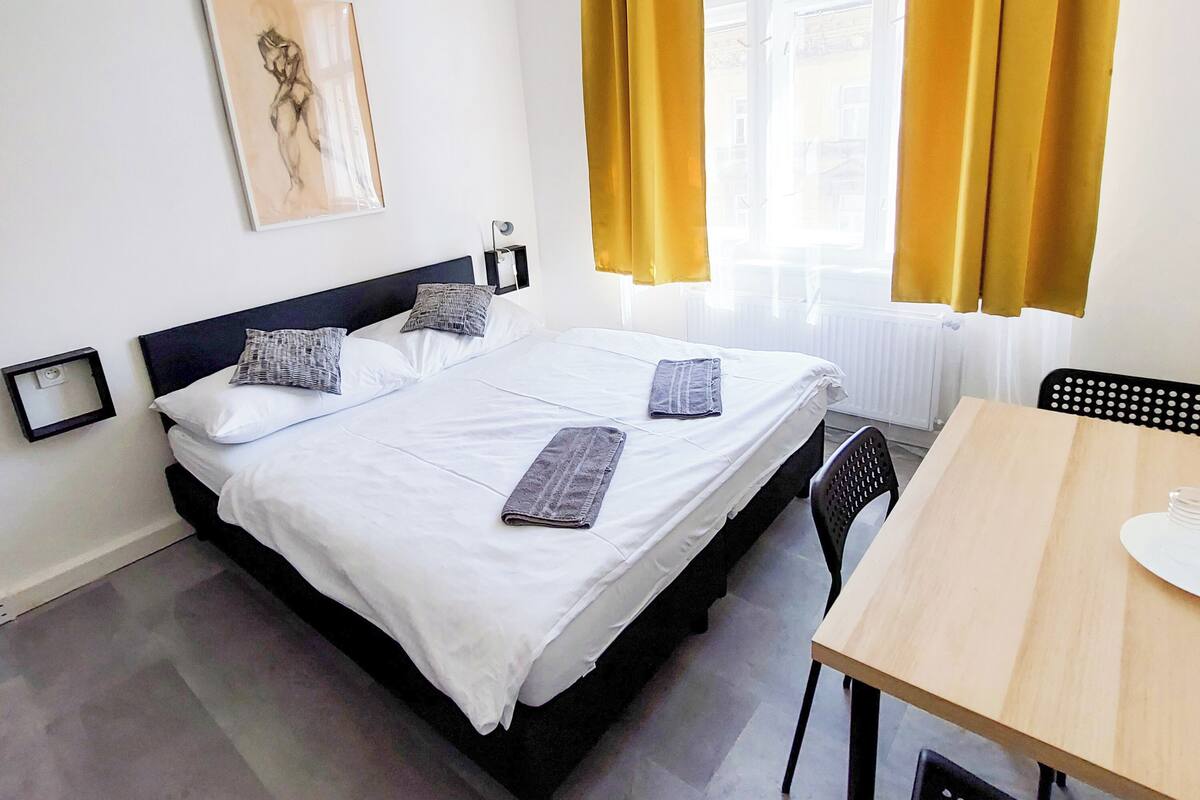 Habitación de hotel con cama, una mesa, sillas, un cuadro en la pared y ventana con cortinas.