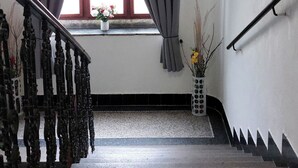 A staircase with a handrail, a window with curtains, and a vase with flowers on the landing. - Milada (Prague)