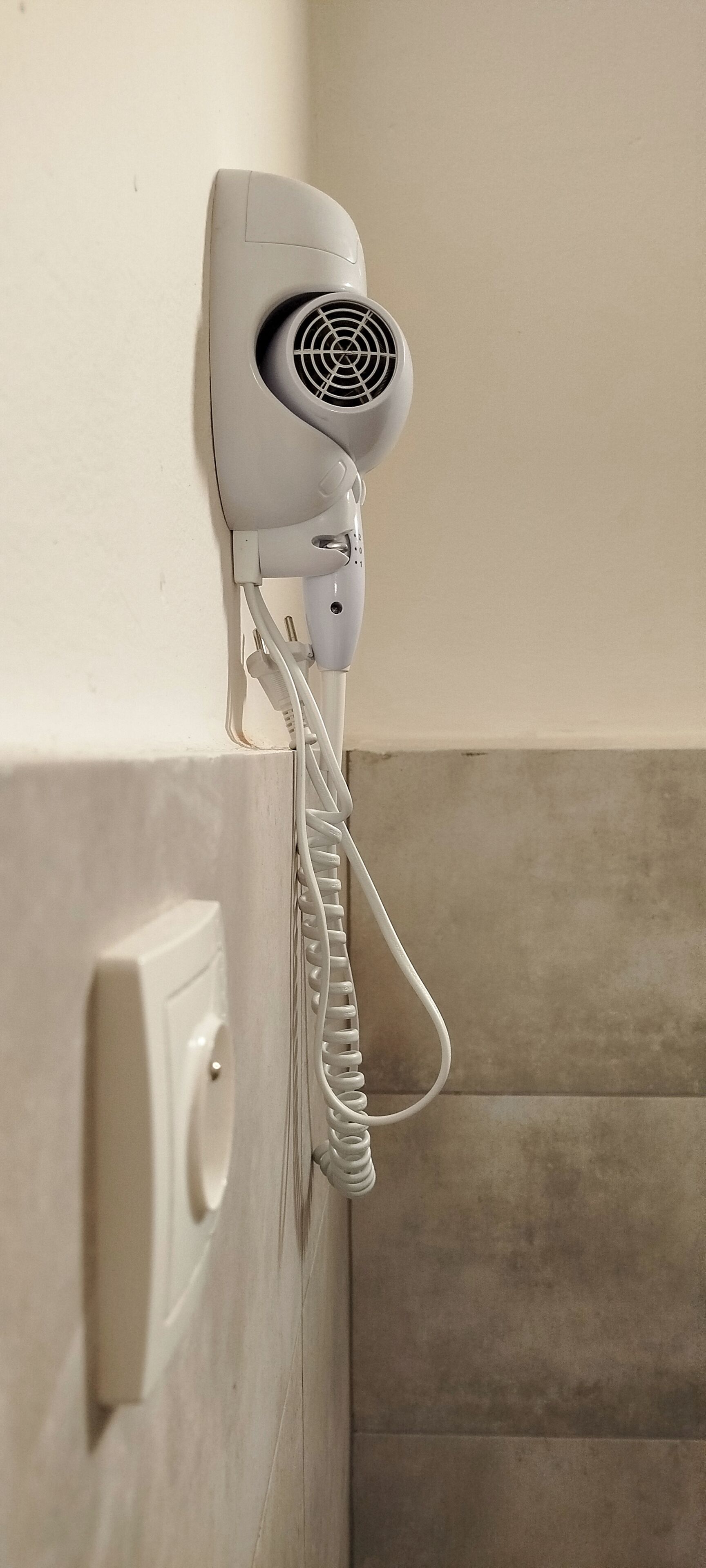 Un secador de pelo montado en la pared con un cable enrollado.