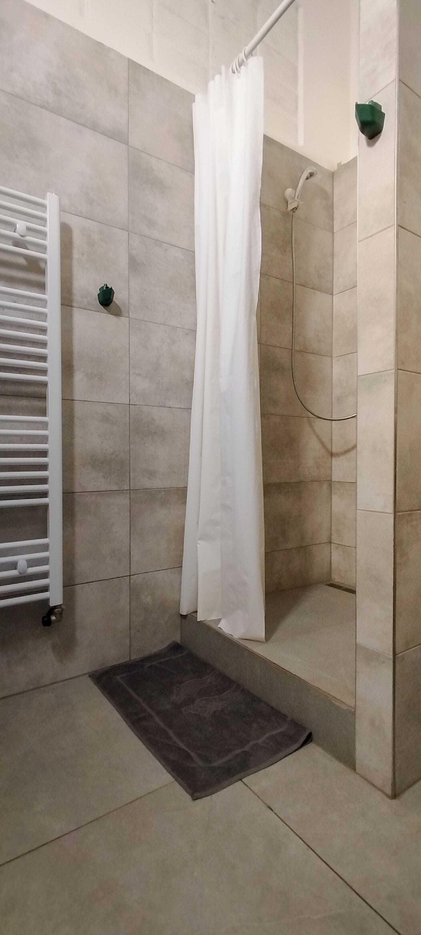 Un espacio de ducha con cortina blanca, cabezal de ducha de mano y un perchero para toallas.