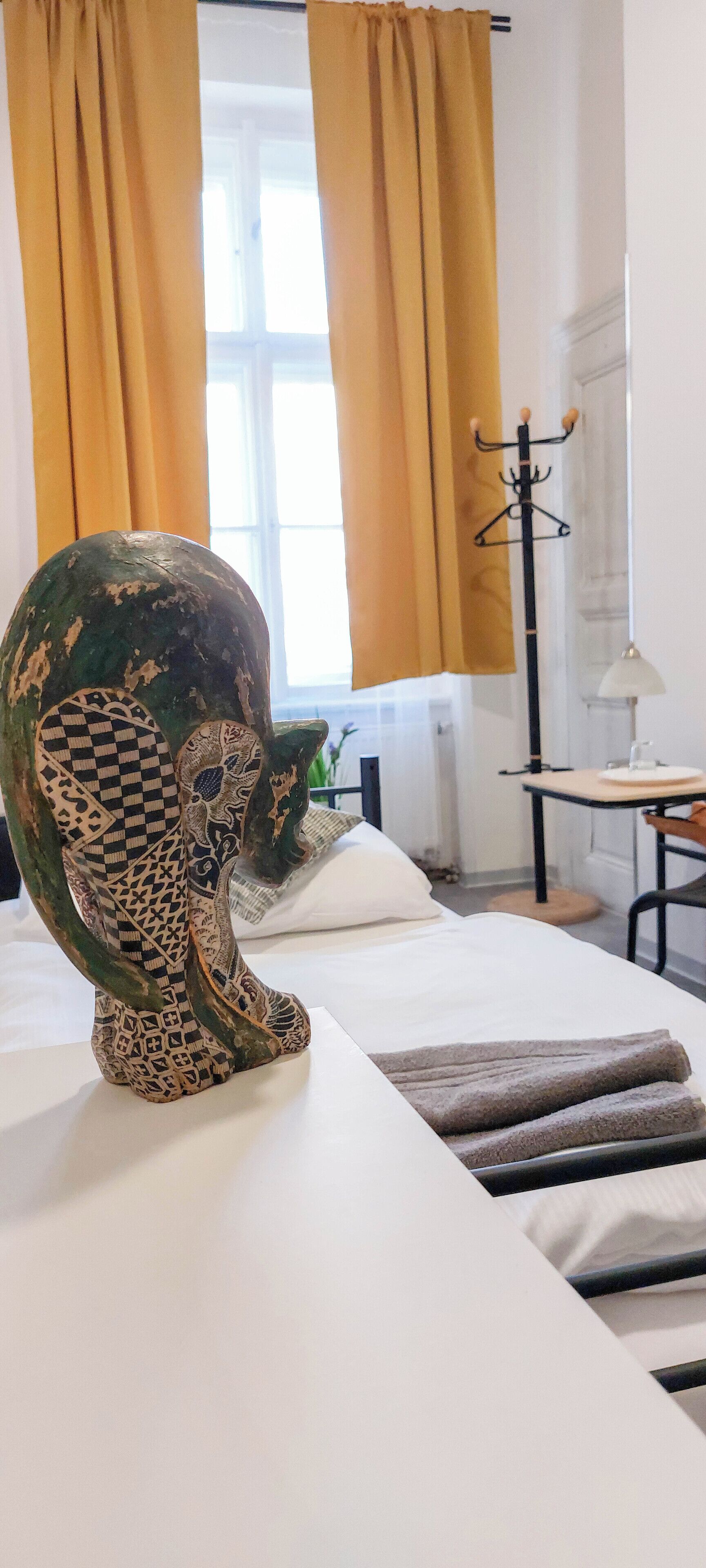 Um quarto com uma cama, uma grande escultura decorativa, um porta-roupas e uma janela com cortinas.