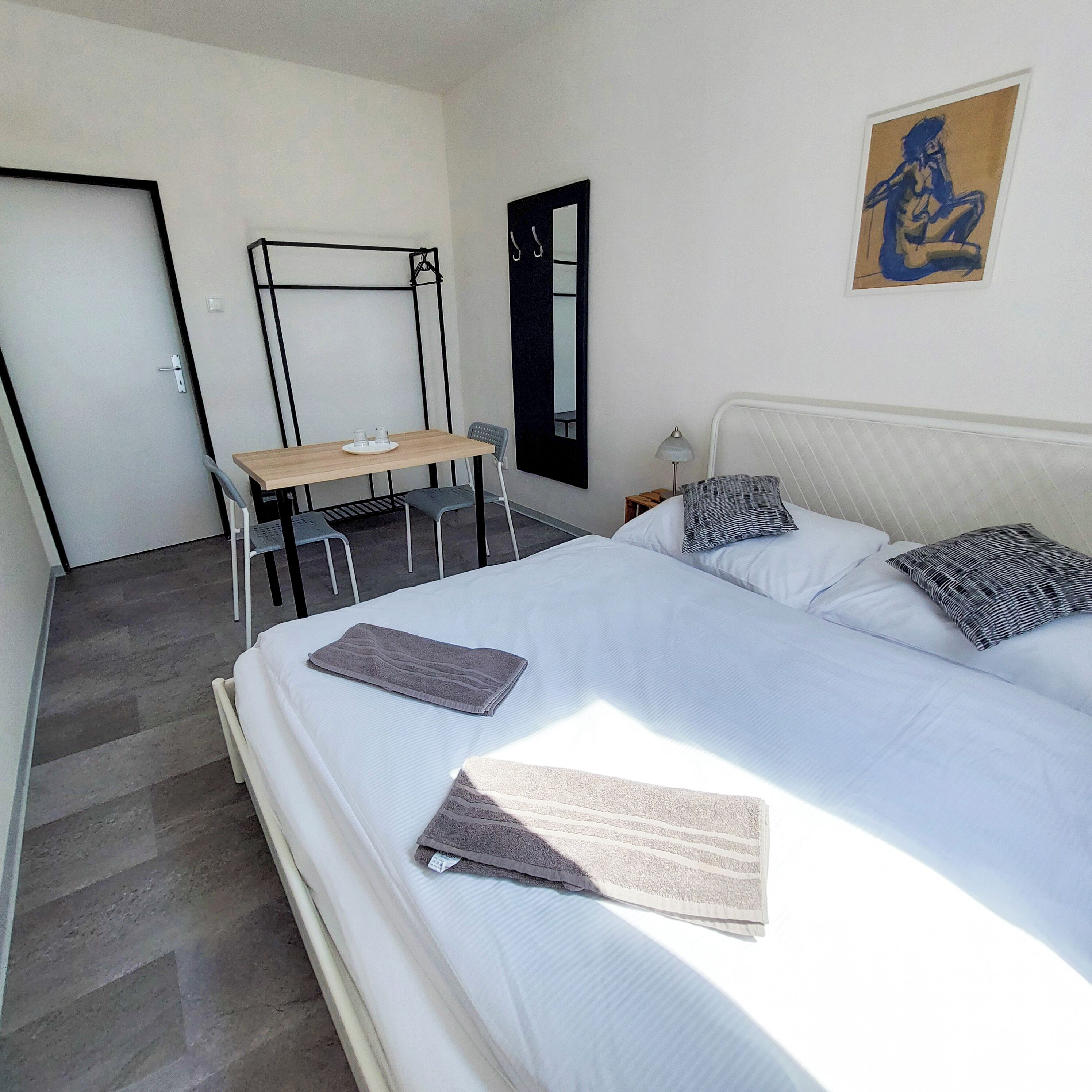 Quarto com cama, escrivaninha e cadeira. Há uma porta e uma janela no aposento.