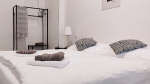 A neatly made bed with pillows and towels, a bedside table with a lamp, and a clothing rack against the wall. - Milada (Prague)
