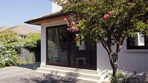 A modern house with a large glass window, a wooden deck, and a tree with pink flowers. - Cómoda Casa con jardín en Las Condes (Santiago)