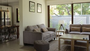 A modern living room with a grey sofa, a coffee table, and a dining area with chairs and a table. - Cómoda Casa con jardín en Las Condes (Santiago)