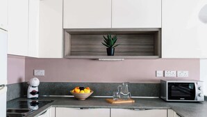A modern kitchen with white cabinets, a built-in oven, a coffee maker, a bowl of fruit, and a potted plant.