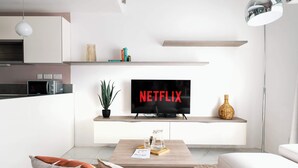 A modern living room with a flat-screen TV on a stand, a coffee table with a glass pitcher, and a small plant.