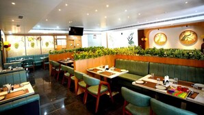 Een restaurant met zitjes en tafels, groen bekleden stoelen en decoratieve wandpanelen.