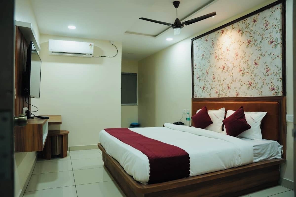 Een hotelkamer met een bed, een plafondventilator, een airconditioning, een houten nachtkastje, een klein krukje en een aan de muur bevestigde televisie.