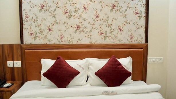 Hotelkamer met bloemenbehang achter het bed, een houten hoofdbord, twee rode kussens en een bed met witte lakens.