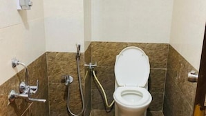 A small bathroom with a toilet, shower, and a red bucket.