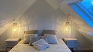 Une chambre avec un plafond en pente, un lit avec des oreillers, deux tables de chevet et des luminaires suspendus.