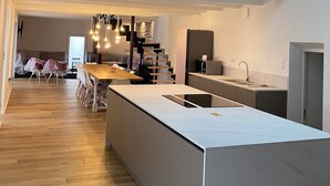 Une cuisine moderne dotée d’un grand îlot central, de planchers en bois et d’un coin repas avec des chaises recouvertes de tissu.