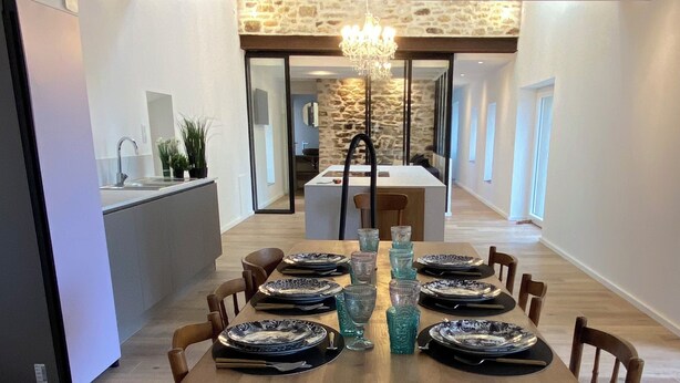 Un coin repas avec une longue table dressée pour six personnes, agrémentée d’assiettes à motifs et de verres en verre transparent.