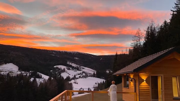 Une cabane en bois dotée d’une terrasse offrant une vue sur un paysage enneigé au coucher du soleil.