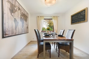Comedor con una mesa de madera dispuesta para cuatro personas, un gran mapa del mundo en la pared y una pizarra con texto.