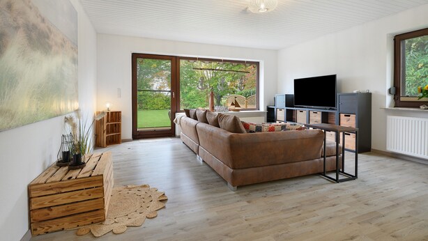 Ein modernes Wohnzimmer mit Sofa, Holzkisten, Fernseher und Blick ins Grüne.