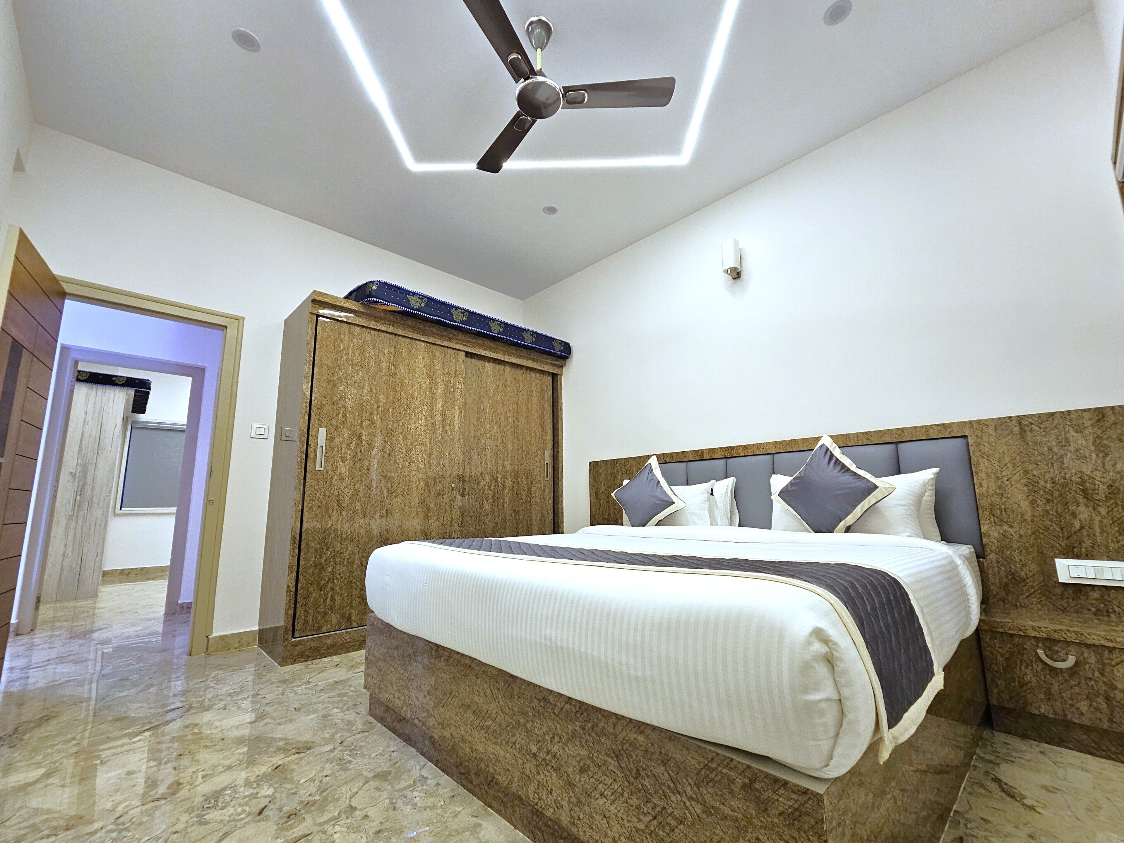 Une chambre à coucher comprenant un lit, un ventilateur de plafond, une armoire et une porte donnant sur une autre pièce.