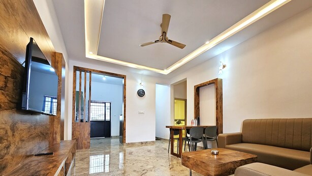Una sala de estar moderna con piso de mármol, muebles de madera, ventilador de techo y un comedor con sillas y una mesa.