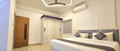 A bedroom with a bed, a ceiling fan, an air conditioning unit, a wardrobe, and a door.