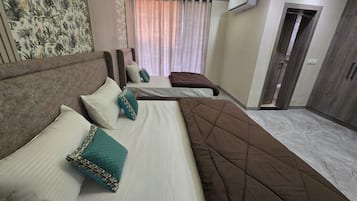 A hotel room with a large bed, two smaller beds, a ceiling fan, an air conditioning unit, and a door leading to another room.