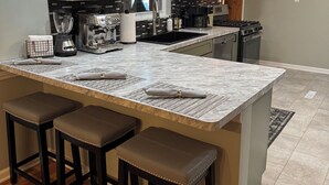 A modern kitchen with white cabinets, a marble island with bar stools, a built-in oven, and a microwave. - Cherry Tree Vacation Home, 4 BR 2 BA 2500 sq ft, safe neighborhood .9 mi to ND! (South Bend)