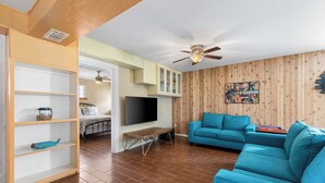 A living room with a blue sofa, wooden flooring, a TV, and a ceiling fan.
