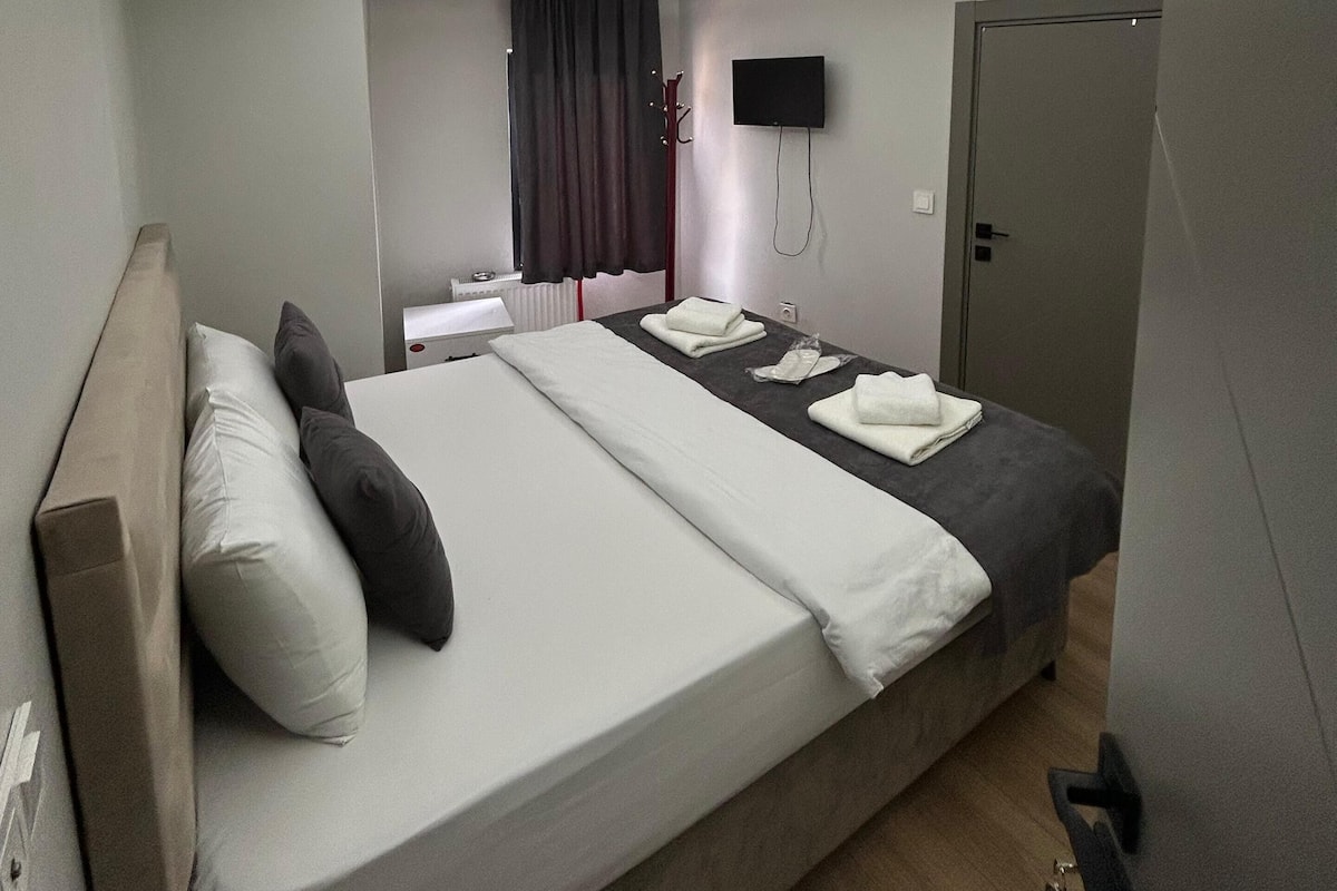 Une chambre d’hôtel moderne avec un grand lit, un téléviseur à écran plat fixé au mur et une porte située sur le côté droit.