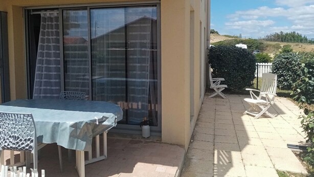 Eine Terrassenfläche mit Tisch und Stühlen, eine Schiebetür und Blick auf einen bewachsenen Hügel.