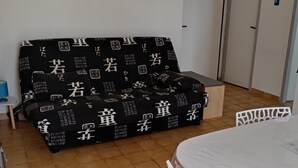 Ein Zimmer mit einer schwarzen Couch mit weißen Mustern, einem weißen Tisch mit einer Kunststoffabdeckung und einem weißen Stuhl.