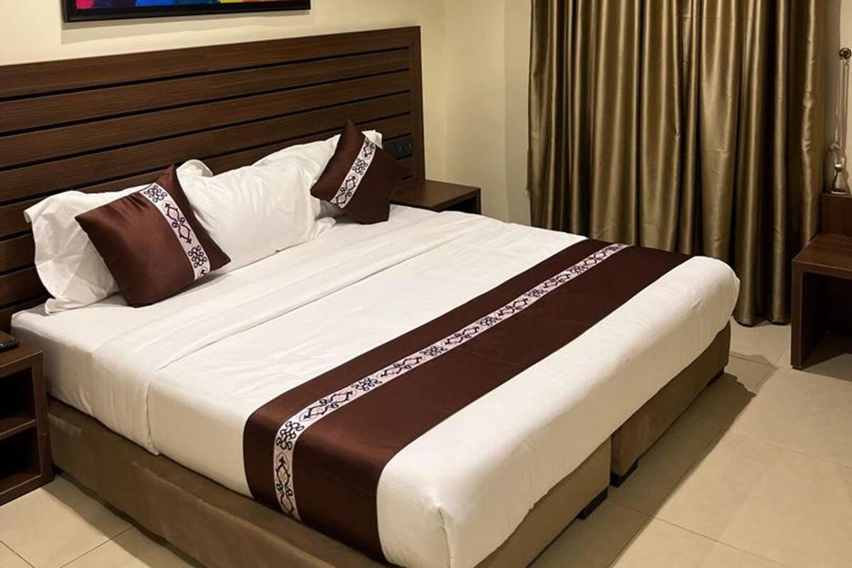A hotel room with a large bed, a headboard, a nightstand, a wall-mounted artwork, and a window with curtains.