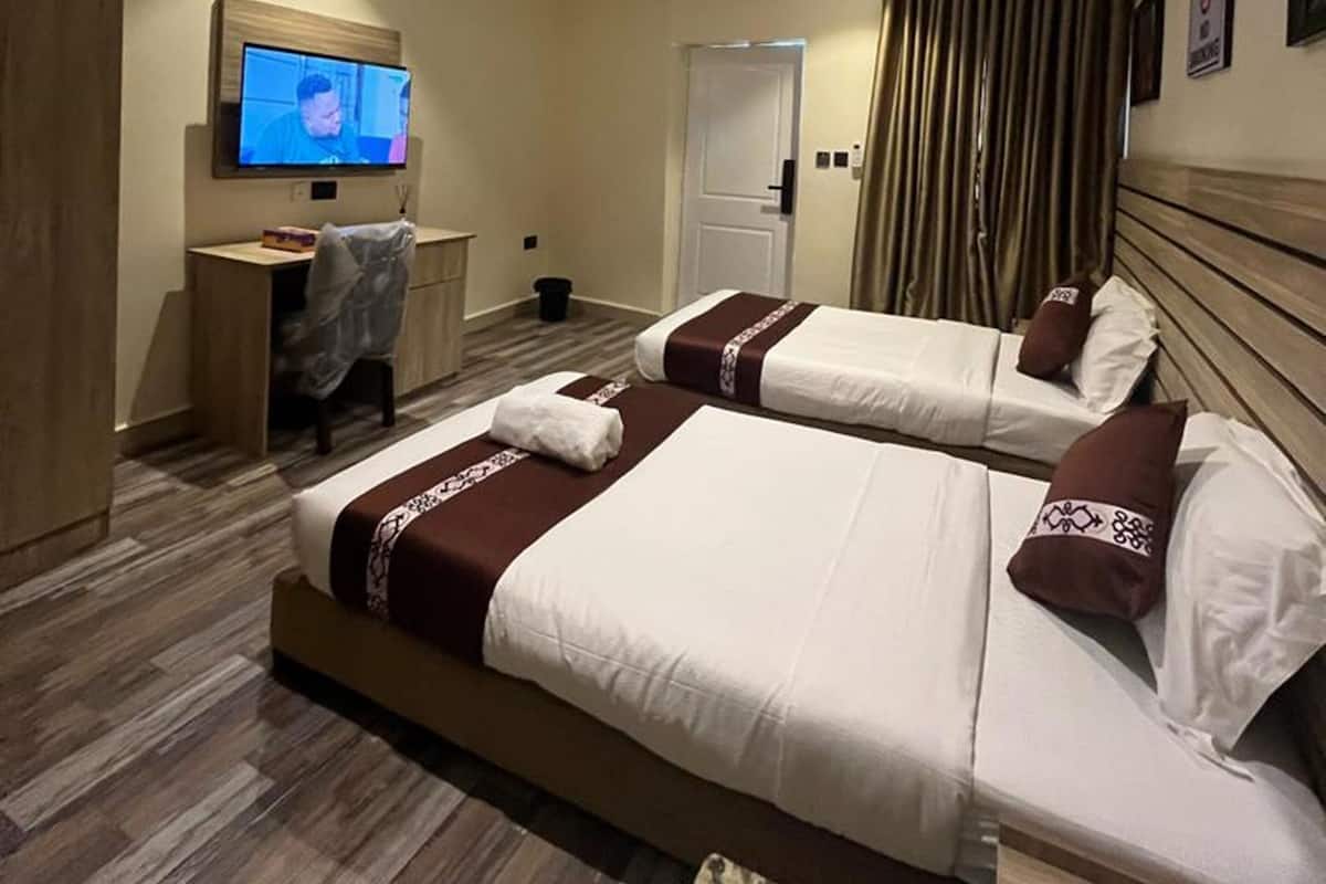 A hotel room with two beds, a desk, a television, and a door.