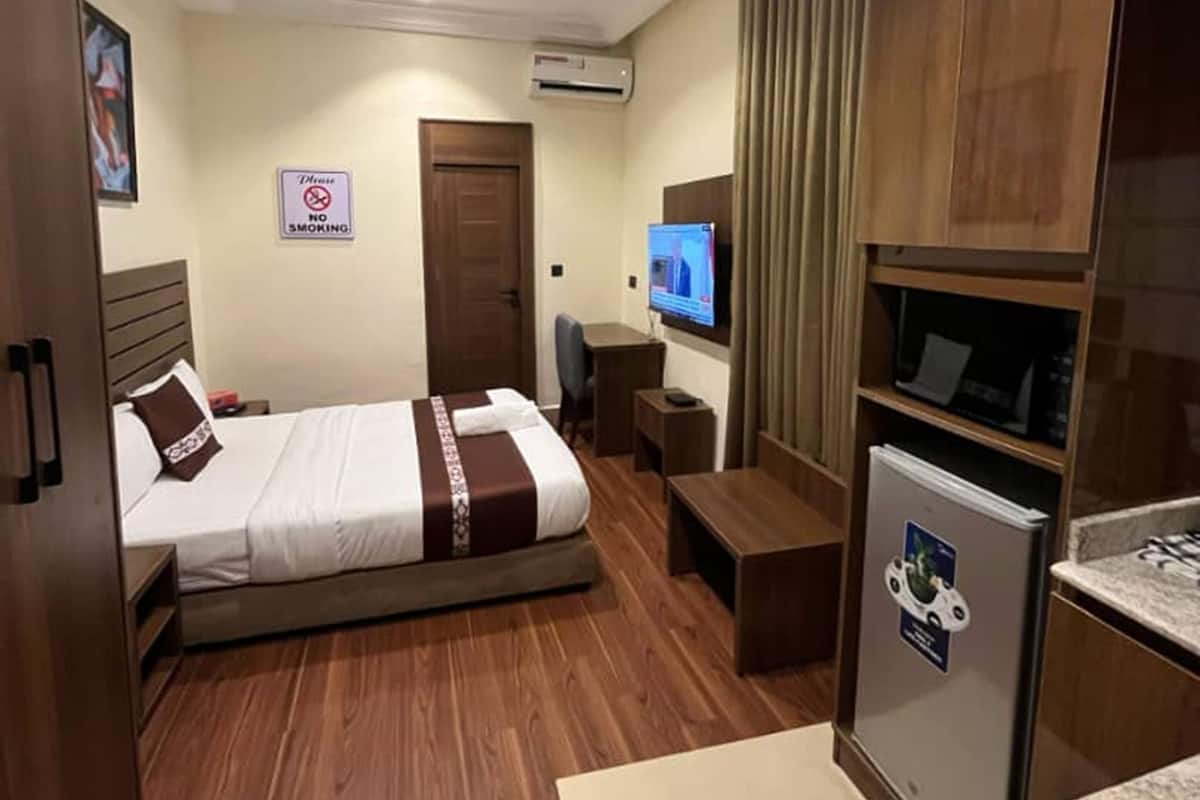 A hotel room with a bed, a desk, a TV, a refrigerator, and a wooden wardrobe.