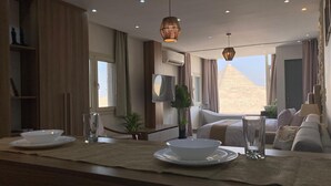 A modern hotel room with a large window, a bathtub, a sofa, and a dining area with plates and glasses. - First Row to Pyramids Studio (Giza Governorate)