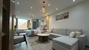 A modern living room with a sofa, a coffee table, and a bed. There is a view of a mountain outside the window. - First Row to Pyramids Studio (Giza Governorate)