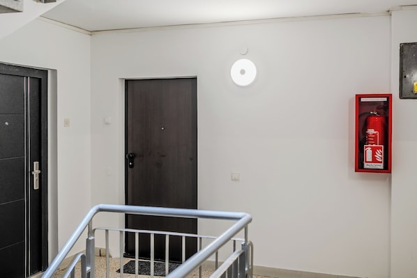 Un pasillo con una puerta de madera oscura, un extintor de incendios sujeto a la pared y una barandilla de metal.