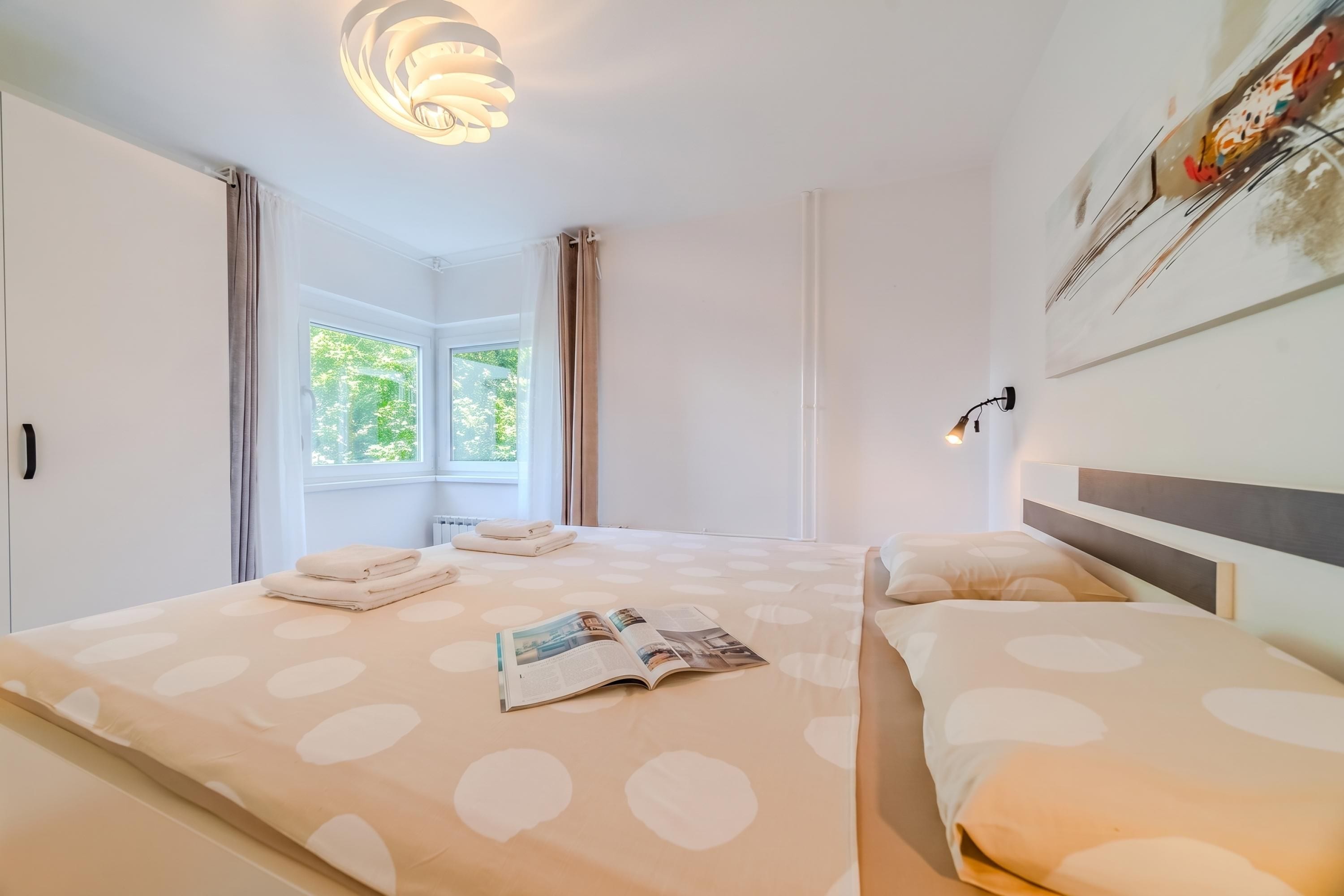 A hotel room with a bed, a window, and a wall-mounted lamp.