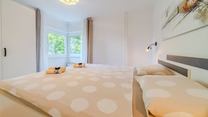 Hotellihuone, jossa on kaksi sänkyä, suuri ikkuna, kattovalaisin ja seinään kiinnitetty lamppu.