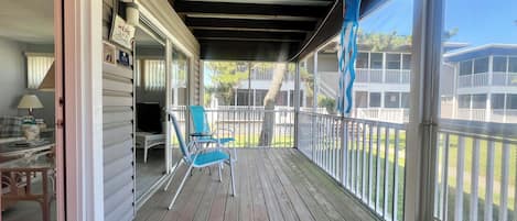 A covered porch with a wooden deck, a seating area with chairs, a television, and a view of neighboring houses.
