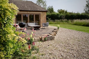 A patio area with outdoor furniture, a barbecue grill, and a stone pathway leading to a building with large windows.