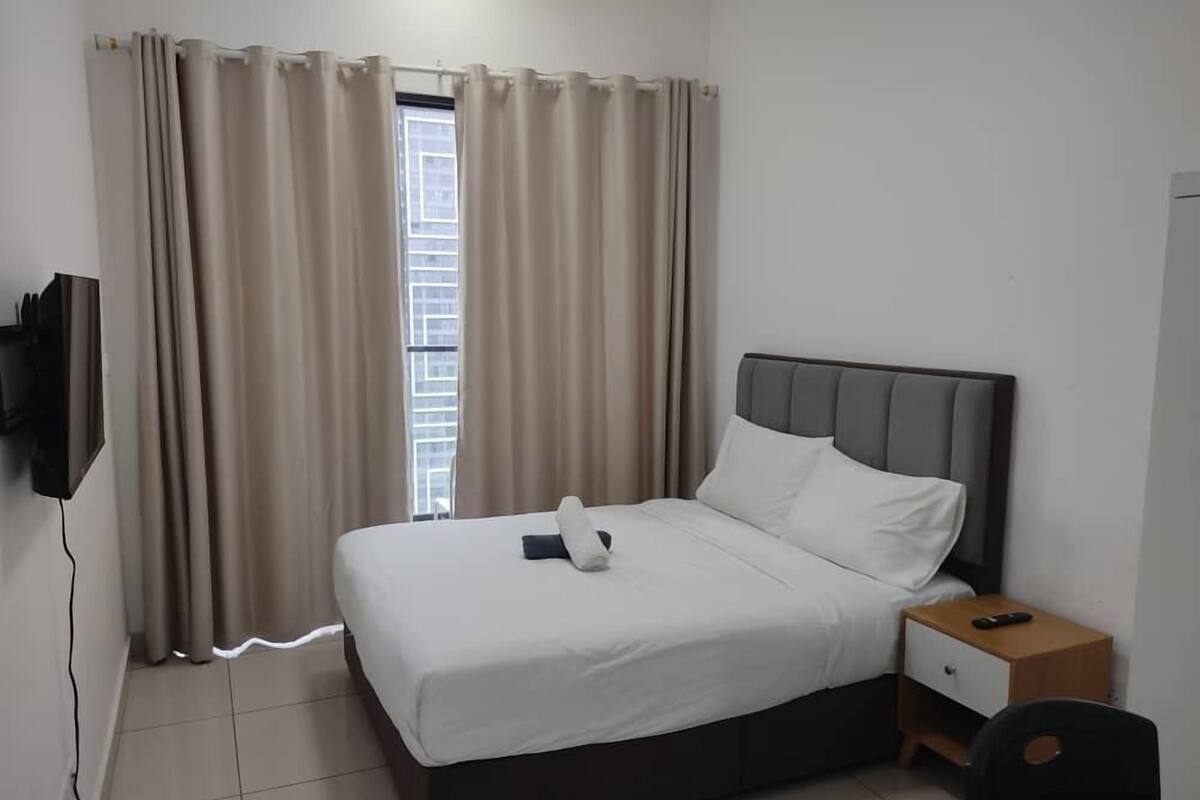Ein Hotelzimmer mit einem Bett, einem Nachttisch, einem an der Wand befestigten Fernseher und einem Fenster mit Vorhängen.
