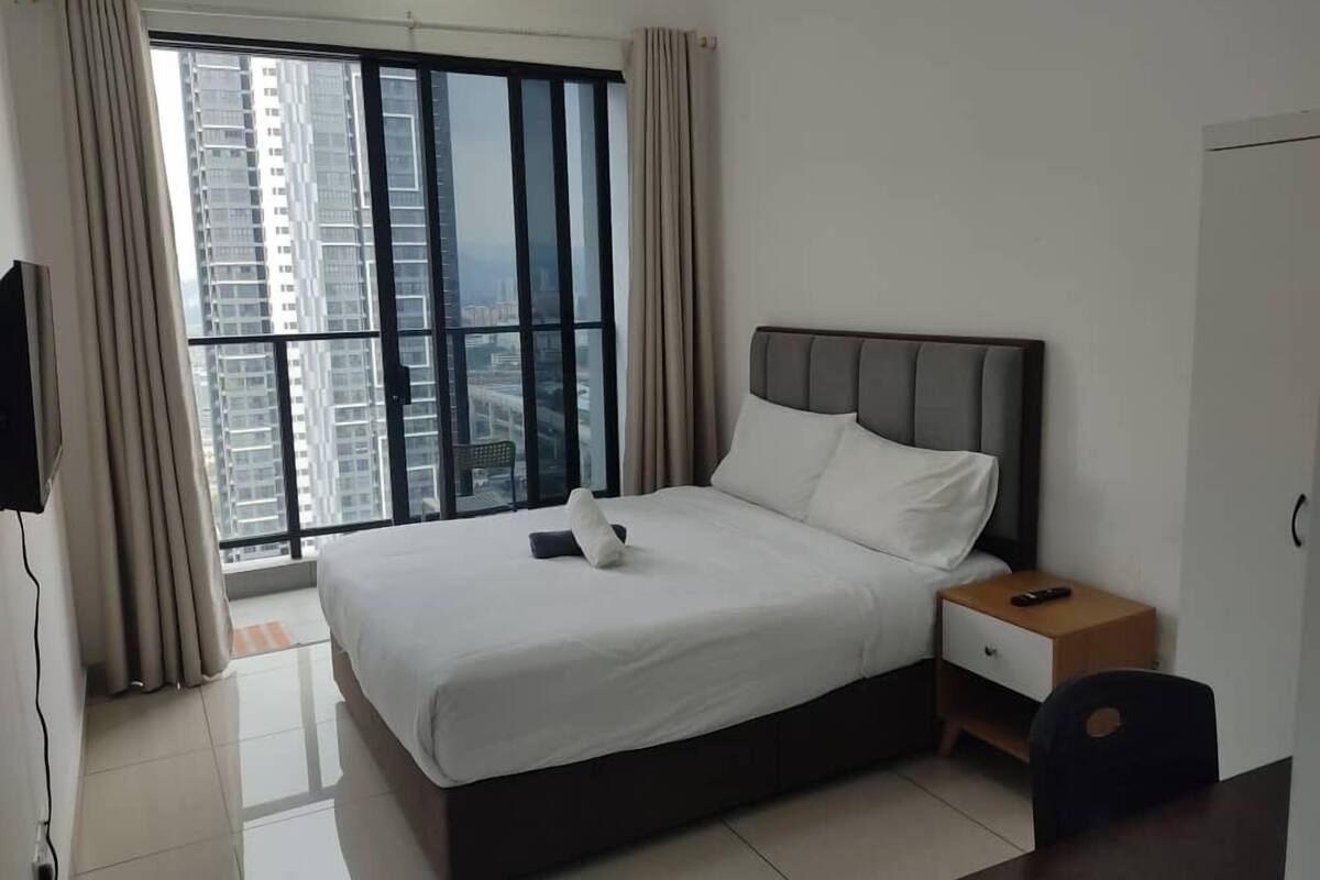 Ein modernes Hotelzimmer mit einem großen Bett, einem Nachttisch, einem Fernseher und Blick auf hohe Gebäude durch das Fenster.