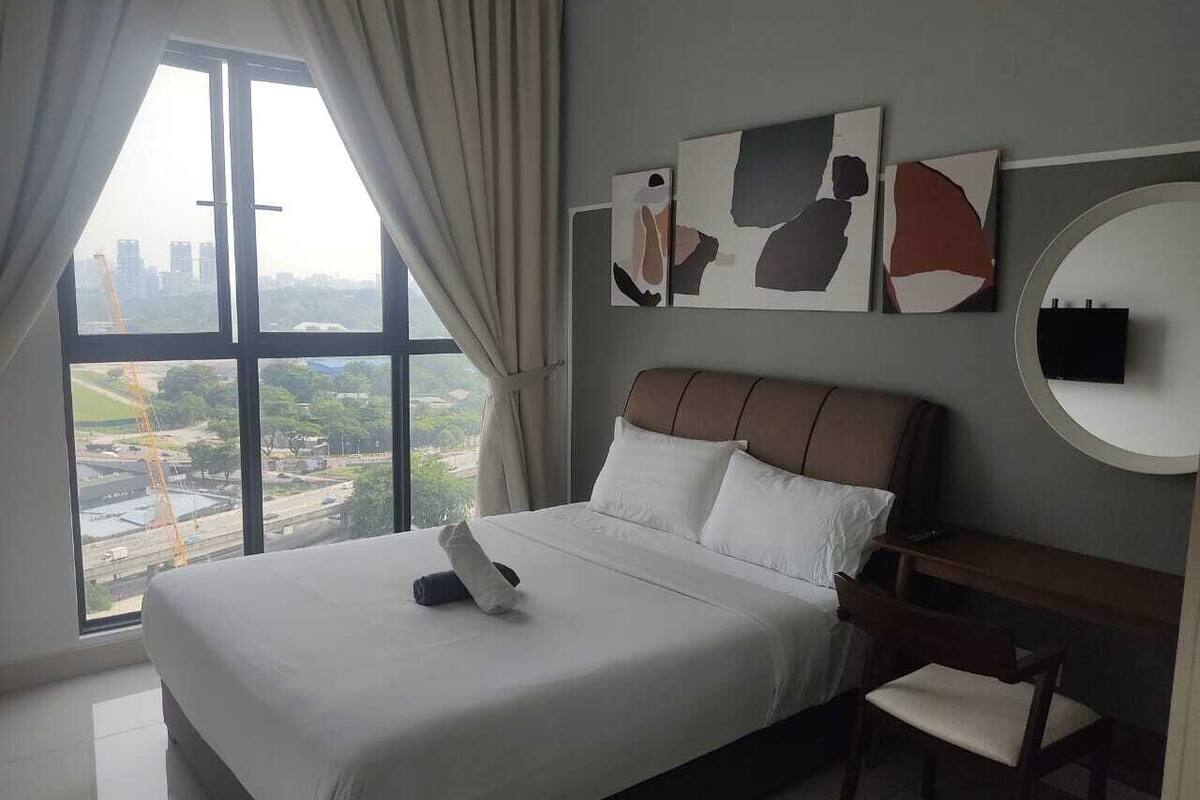 Ein Hotelzimmer mit einem großen Bett, einem Schreibtisch und Blick auf eine Stadtlandschaft durch ein großes Fenster.
