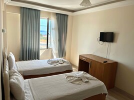 Habitación de hotel con dos camas, un escritorio de madera, un televisor y una ventana con cortinas.