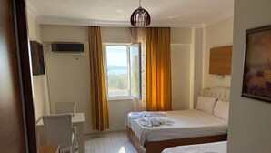 A hotel room with two beds, a desk, a chair, a window with curtains, an air conditioning unit, and a painting on the wall. - GRAND ALVER OTEL (Edremit)