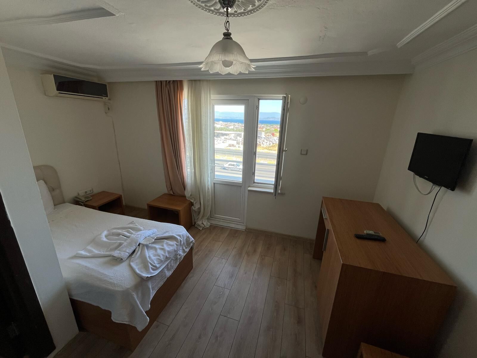 A bedroom with a bed, bedside tables, a desk, a TV, and a window with a view.
