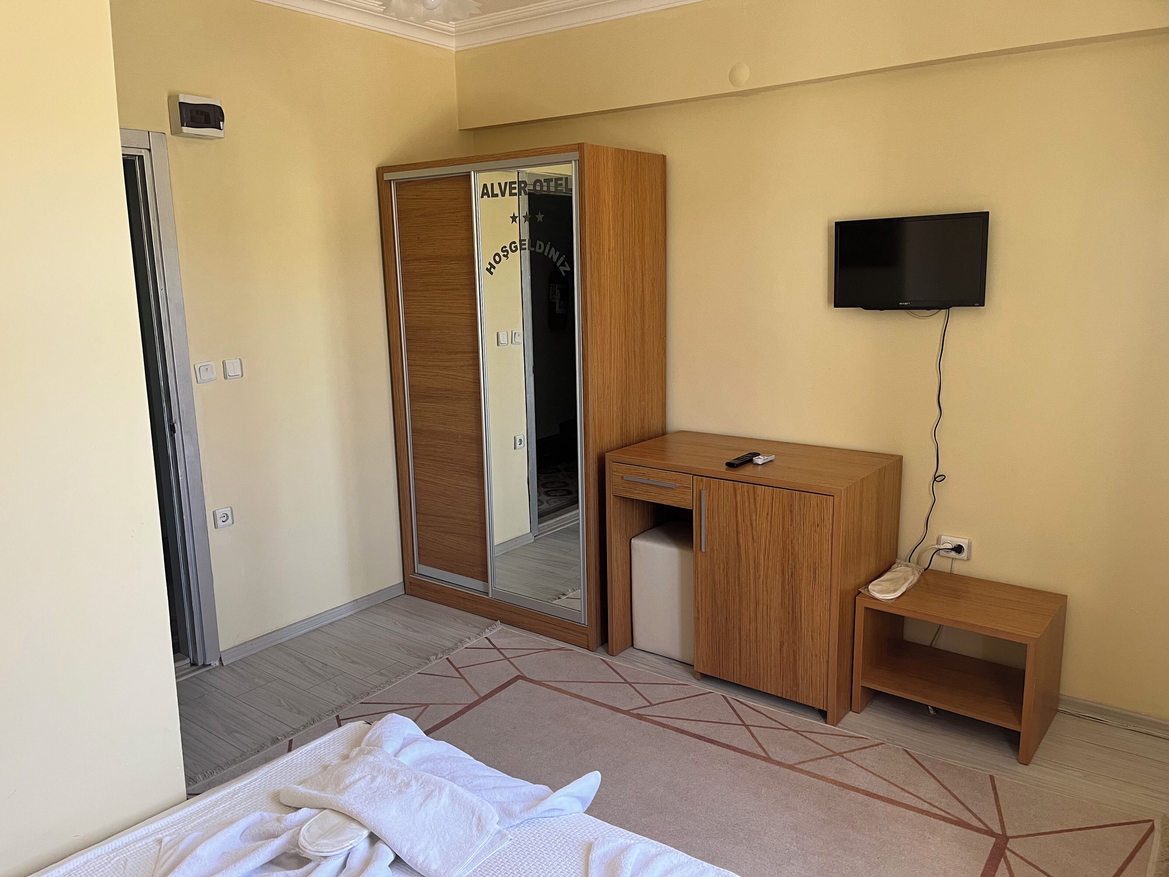 Una habitación de hotel con una cama, un escritorio de madera, un espejo, un televisor y una mesita.