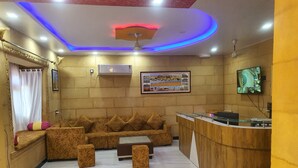 A hotel lobby with a sofa set, a reception desk, and a ceiling with blue lighting.