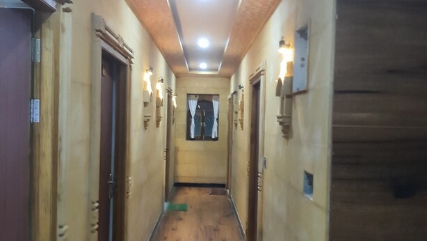 A narrow hallway with wooden flooring, doors on both sides, and a trash bin in the center.