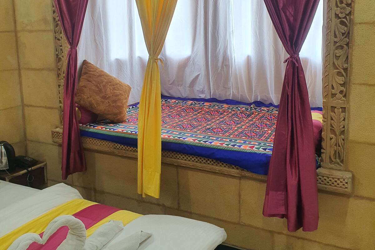 A hotel room with a bed, a window with curtains, a bedside table, and a wall with a decorative pattern.